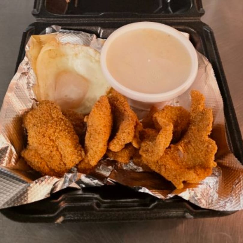 Southern Stop's fried catfish, grits, and gravy in a black to-go container lined with foil.