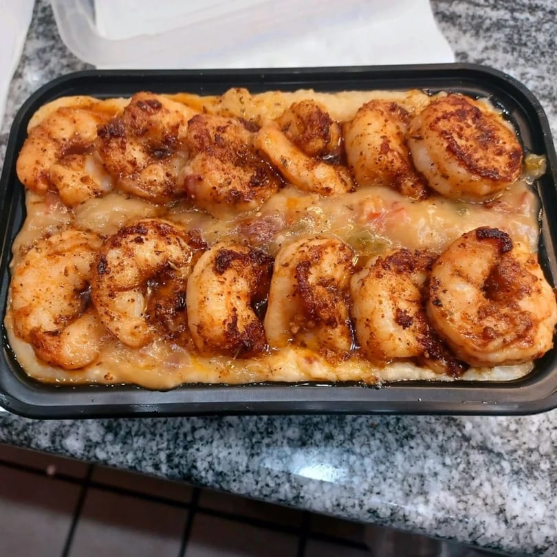 Southern Stop's shrimp and grits, featuring seasoned shrimp atop creamy grits in a black container.