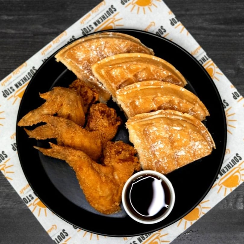 Southern Stop's fried chicken wings and powdered sugar waffles with syrup on a black plate.